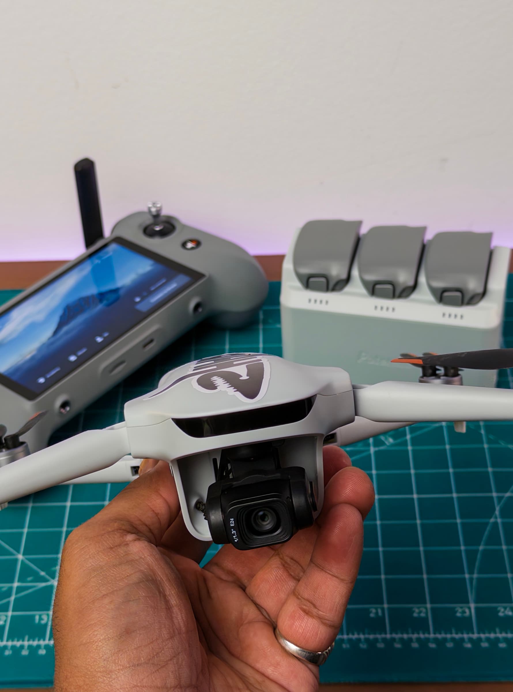 Potensic ATOM 3 held in a hand, gimbal camera facing forward, with its controller and battery charging hub behind