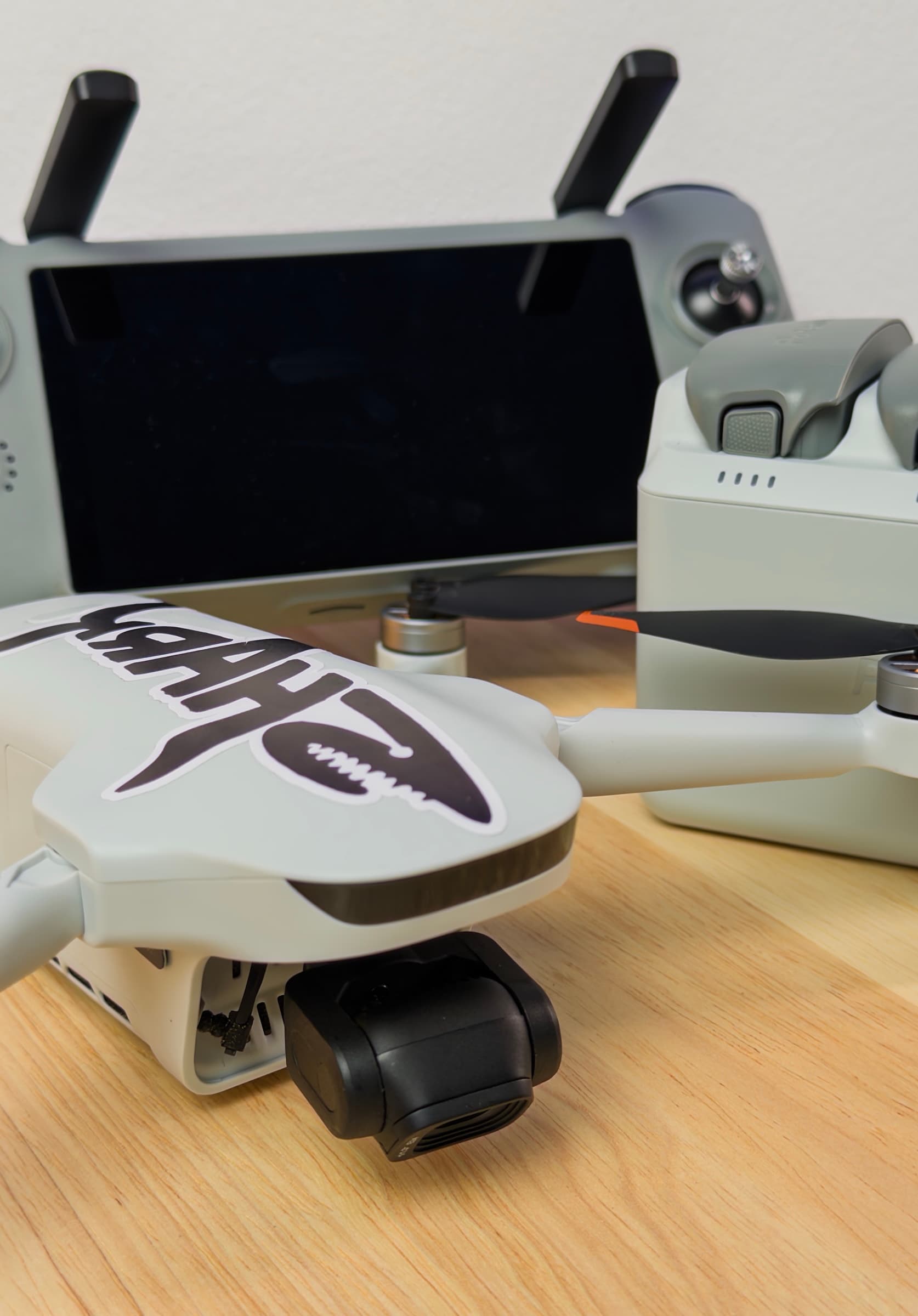 Potensic ATOM 3 with a shark graphic on a wooden table, gimbal camera in front and its controller and battery hub behind