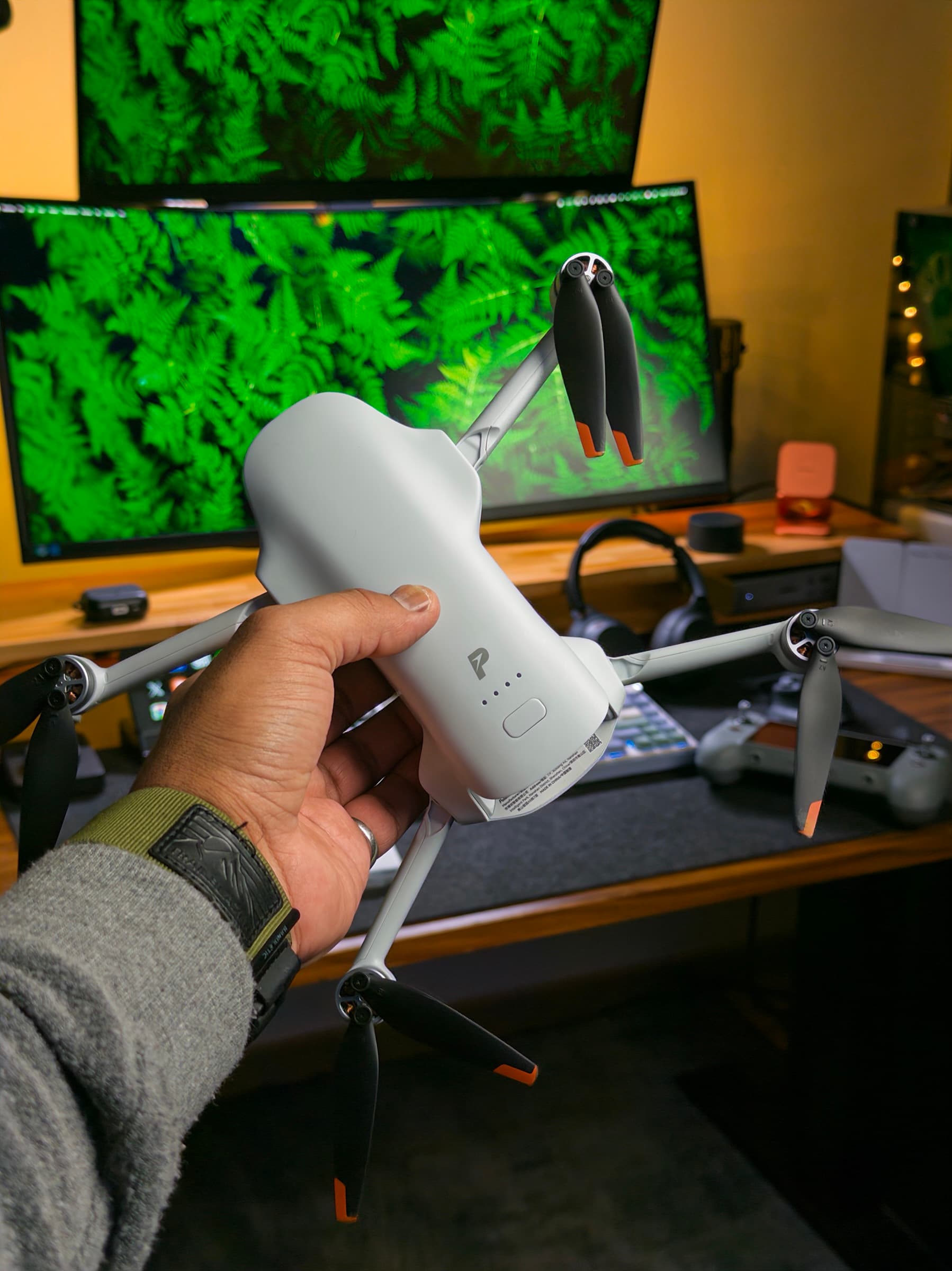 Potensic ATOM 3 held in a hand with its arms unfolded, in front of a desk with two monitors