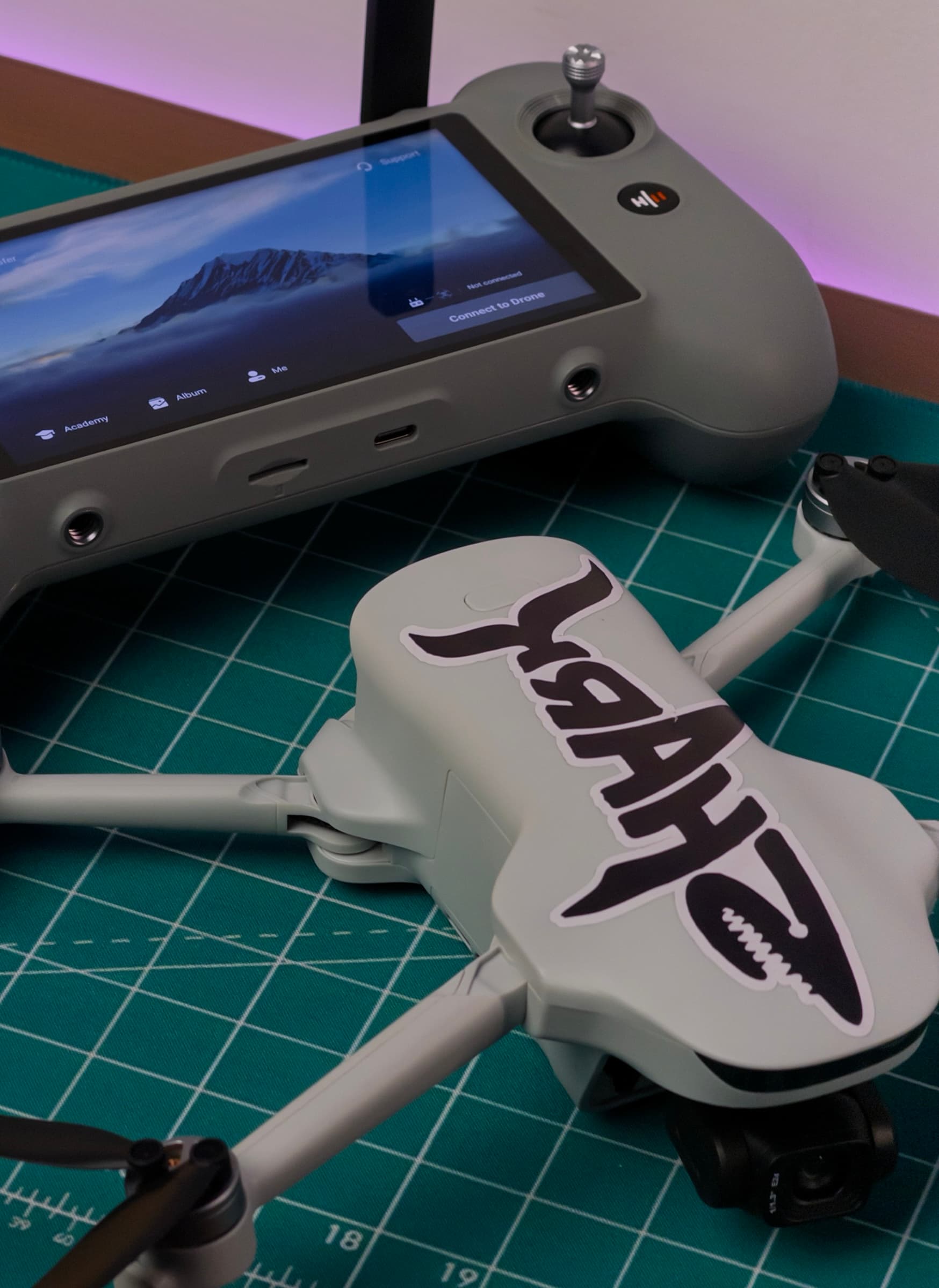 ATOM 3 with arms unfolded and a shark graphic on top, beside its touchscreen controller on a cutting mat
