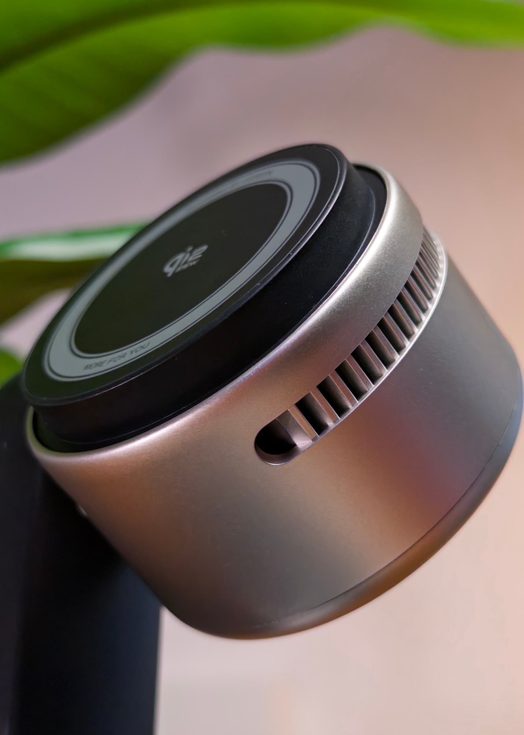 Close-up of the MagFlow Pro's Qi2 charging pad and vented aluminium housing beneath plant leaves